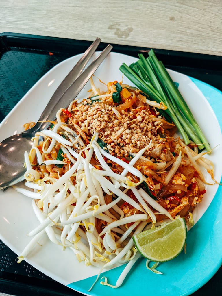 A delicious plate of traditional Thai Pad Thai garnished with fresh vegetables and lime wedge.