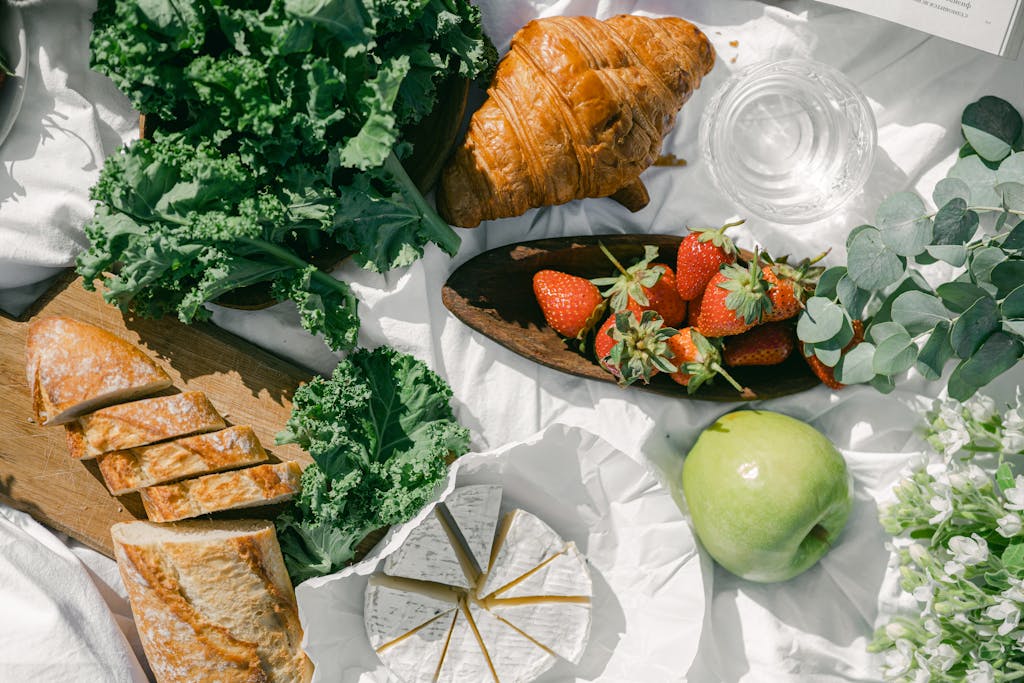 A vibrant picnic spread featuring bread, croissant, strawberries and fresh greens.