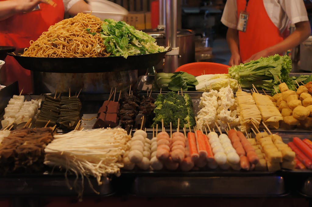Colorful Asian street food display with assorted skewers and fresh vegetables under warm lighting.
