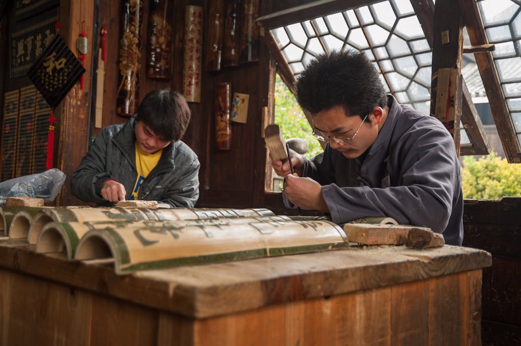Two artisans meticulously carving bamboo pieces in a traditional workshop in Guilin, Guangxi, China.